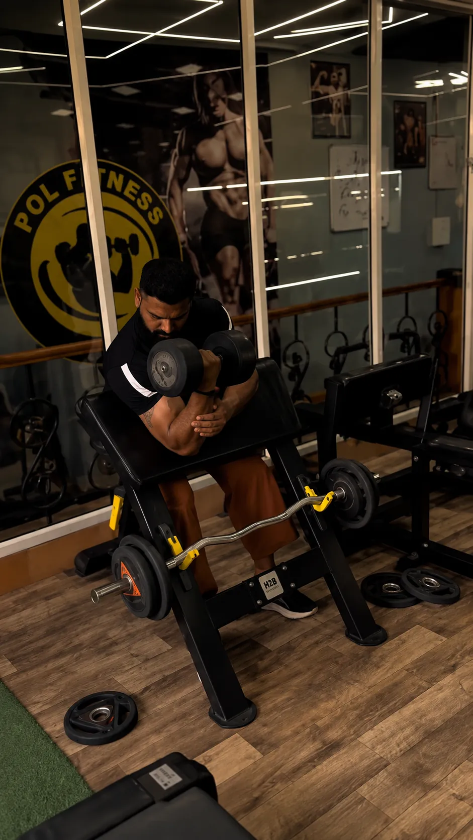 Preacher curl in front of the POL Fitness logo wall